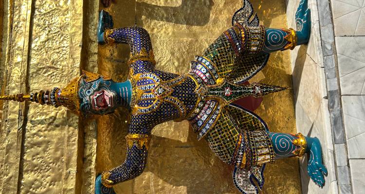 Estatua guardiana colorida frente a una pared dorada de templo.