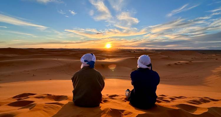 Deux individus regardant le coucher de soleil sur les dunes du désert.