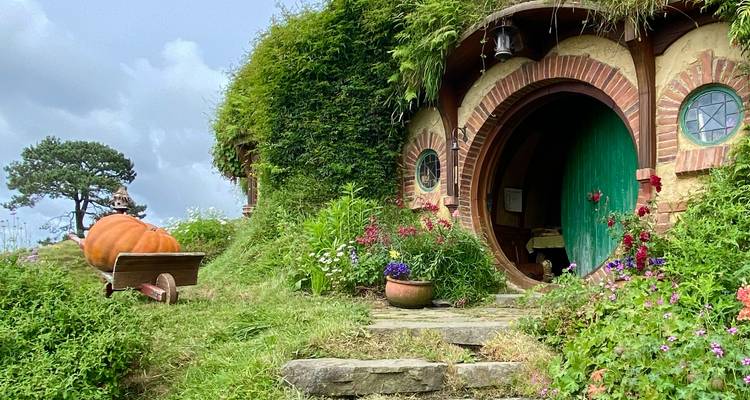 Porte de hobbit pittoresque entourée de verdure et de fleurs colorées.