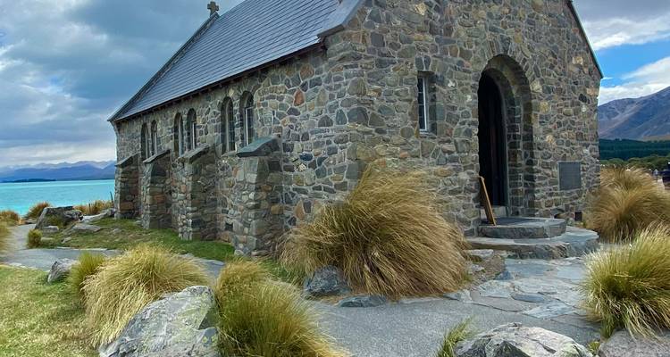 Église en pierre près d'un lac sous un ciel partiellement nuageux.
