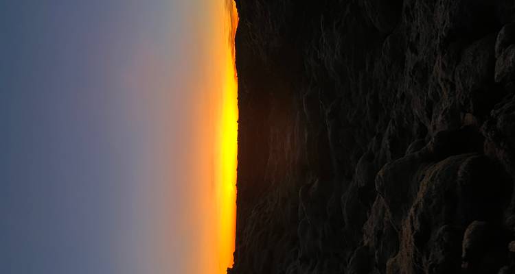 Coucher de soleil sur un terrain rocheux avec un ciel orange.