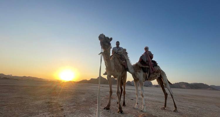 Deux personnes chevauchant des chameaux au coucher du soleil dans un paysage désertique.