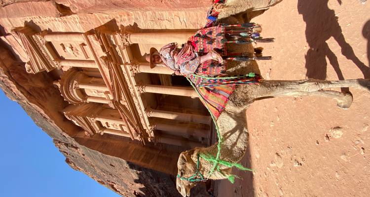 Personne sur un chameau devant une architecture ancienne taillée dans la roche.
