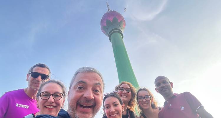 Groupe posant avec une haute tour en arrière-plan sous un ciel bleu.