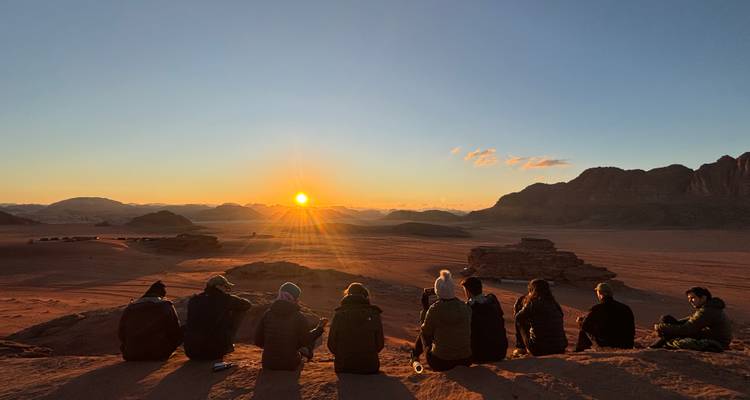 Des gens assis sur une crête regardant le coucher de soleil sur un paysage désertique.