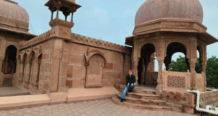 Hombre sentado en un sitio histórico con estructuras abovedadas.