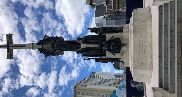 Oorlogsmonument met standbeelden en hoge, historische gebouwen op de achtergrond.
