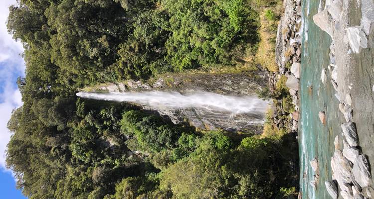 Una cascada alta cayendo por un acantilado rocoso rodeada de bosque.