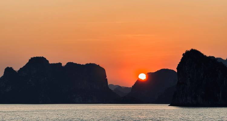 Vista del atardecer sobre paisajes kársticos y agua, creando un efecto de silueta.