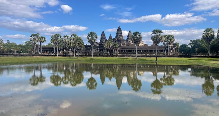Temple d'Angkor Vat reflété dans l'eau entouré de palmiers.