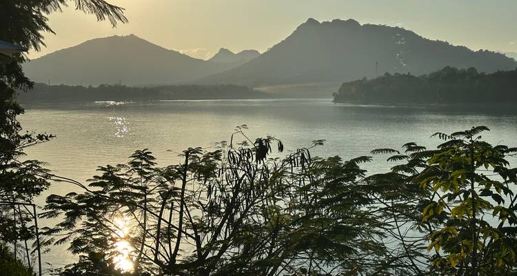 Lago sereno rodeado de montañas bajo un sol poniente.
