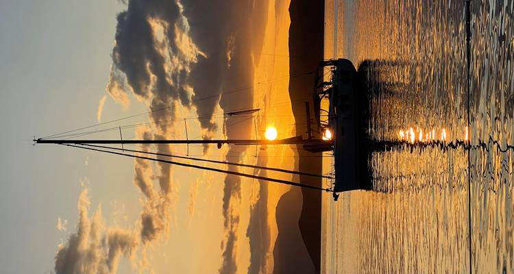 Velero silueteado contra el sol poniente.