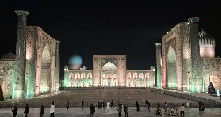 Registan Square with illuminated madrasahs and domes at night.