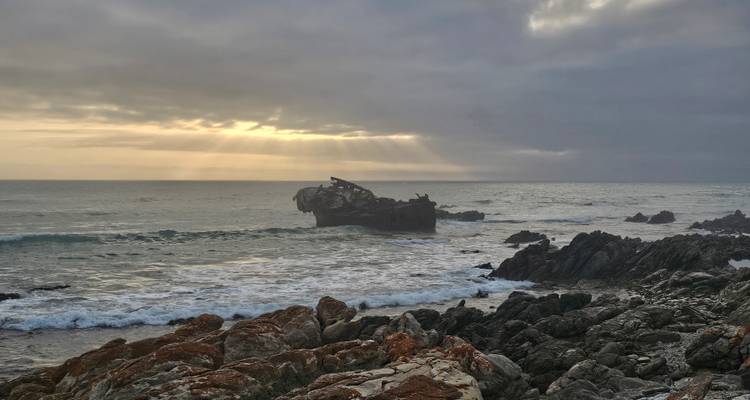 Vue panoramique sur l'océan avec une épave et un ciel dramatique.