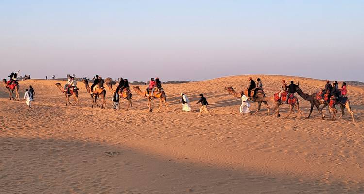 Des gens chevauchant des chameaux à travers les dunes de sable.