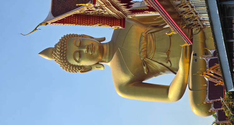Gran estatua dorada de Buda junto a un templo bajo un cielo azul.