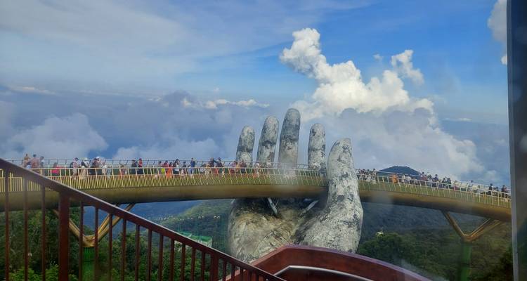 Puente Dorado con grandes esculturas de manos y nubes de fondo.