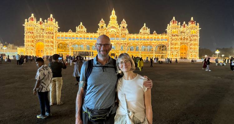 Un couple debout devant un palais brillamment éclairé la nuit.