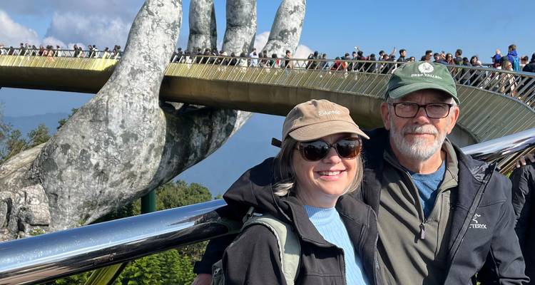 Pareja parada frente al Puente Dorado con manos gigantes.