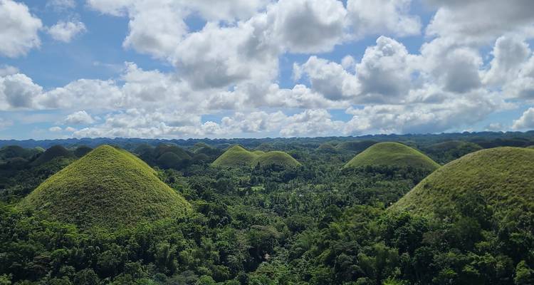Une vue panoramique des Chocolate Hills sous un ciel nuageux.