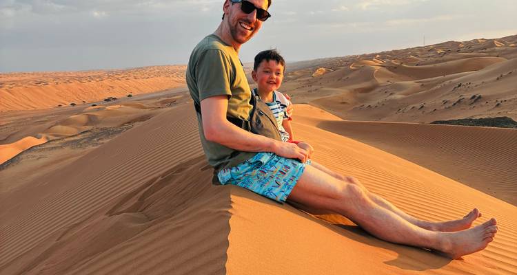 Homme et enfant assis sur une dune de sable profitant de la vue.