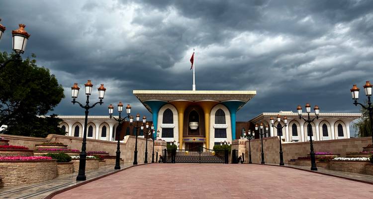 Grand palais avec ciel dramatique, montrant drapeaux et fleurs.