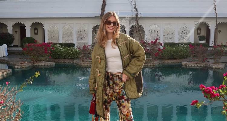 Une femme qui pose dans un jardin avec une piscine devant un bâtiment décoré.