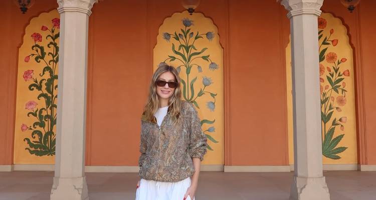 Une femme posant dans un couloir peint de couleurs vives avec des décorations florales.