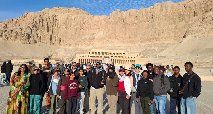 Group of tourists standing in front of an ancient rock-cut temple.