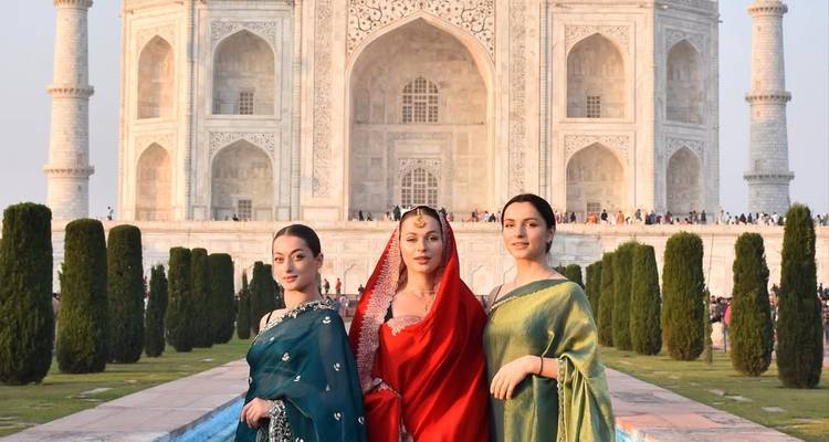 Drei Menschen in traditioneller Kleidung stehen vor dem Taj Mahal.