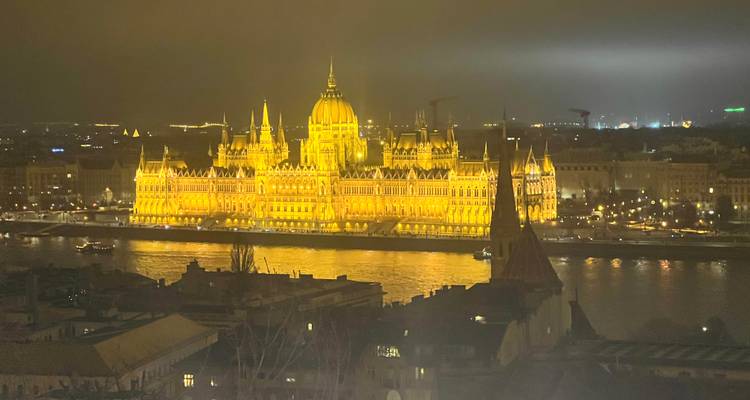 Vista nocturna de un gran edificio iluminado junto a un río.