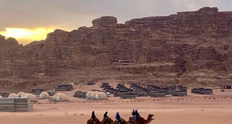 Des gens chevauchant des chameaux dans un paysage désertique avec des tentes.