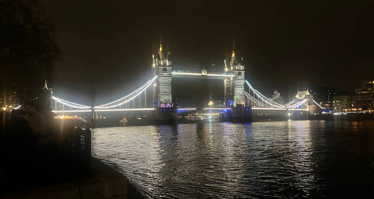 El Puente de la Torre iluminado por la noche, reflejándose en el río Támesis.