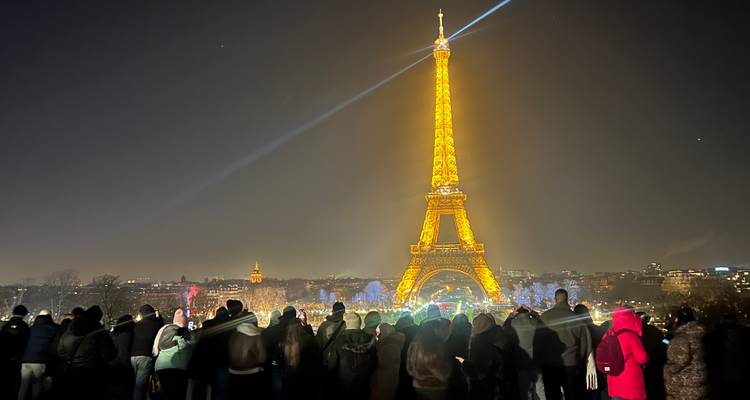 Torre Eiffel brillantemente iluminada por la noche con una multitud de personas reunidas.
