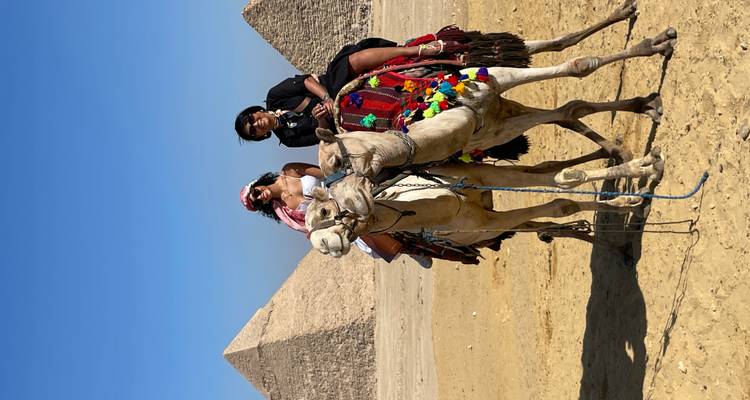 Deux personnes sur des chameaux avec des pyramides en arrière-plan.