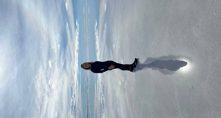 Una mujer parada en salares reflectantes con el cielo reflejado en el agua.