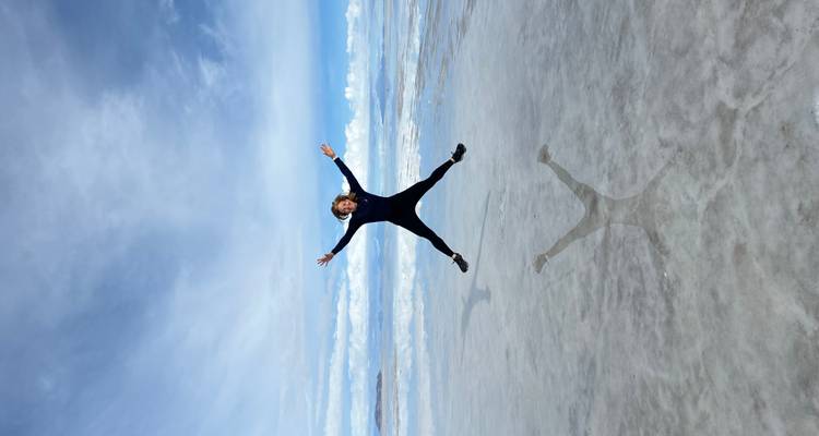 Una mujer saltando en el aire en salinas con su reflejo.