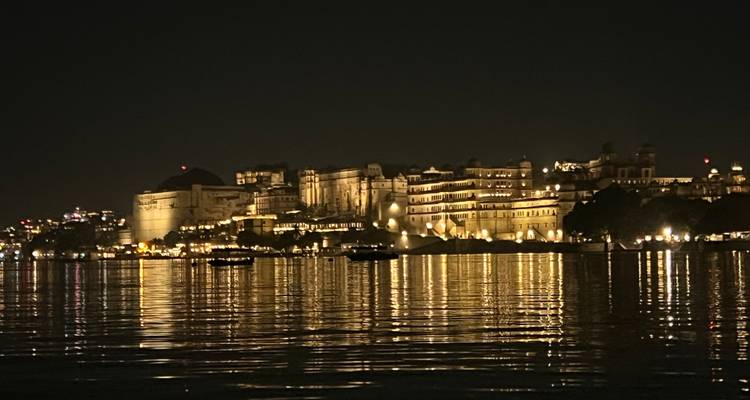 Palastkomplex nachts beleuchtet, spiegelnd auf dem Wasser.