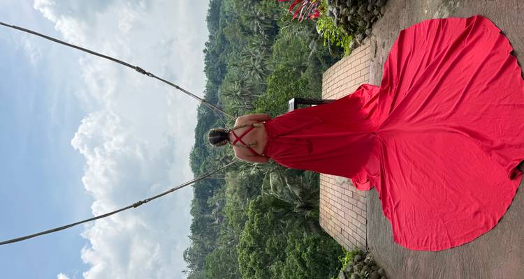 Une personne en robe rouge saisissante sur une balançoire surplombant une végétation luxuriante.