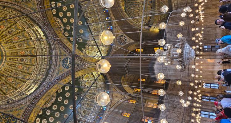 Interior de una mezquita histórica con un techo ornamentado y numerosos visitantes.