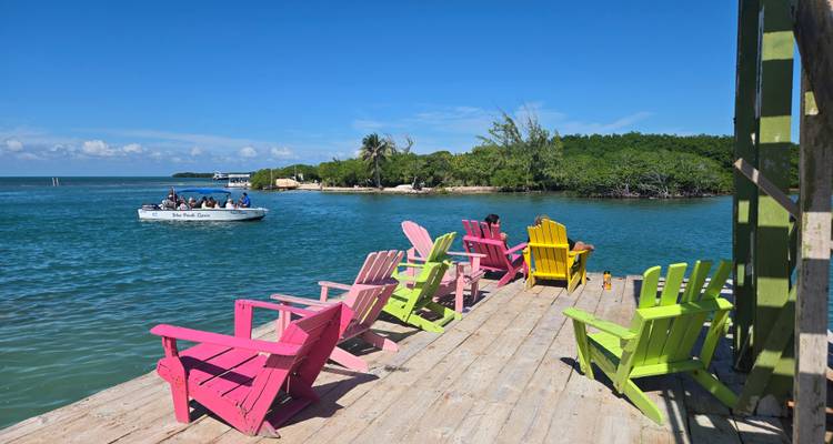 Tumbonas coloridas en un muelle de madera junto al mar con un barco en el agua.