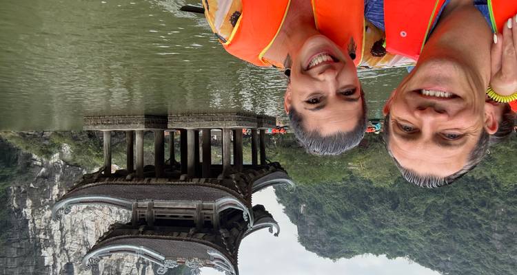 Un couple portant des gilets de sauvetage dans un bateau avec une pagode et une falaise calcaire en arrière-plan.