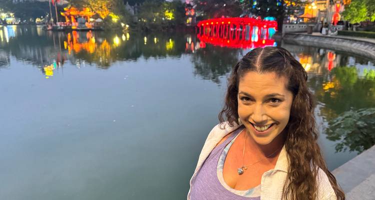 Une femme debout près d'un plan d'eau avec des lumières de pont rouge vif reflétées sur l'eau.