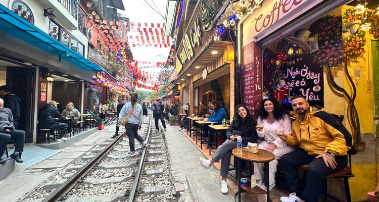Una escena callejera animada con cafés y decoraciones, con una vía férrea que la atraviesa.