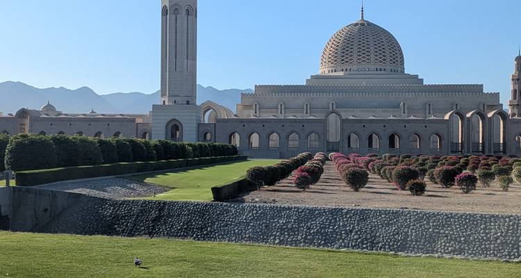 Gran mezquita con diseños intrincados rodeada de jardines y montañas al fondo.