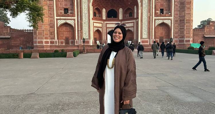 Besucher posiert vor einem großen roten Sandsteintor.