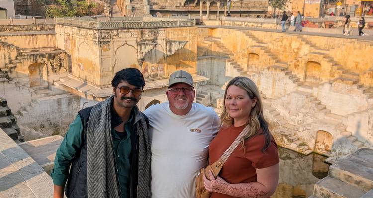 Tres personas posando frente a un pozo escalonado histórico.