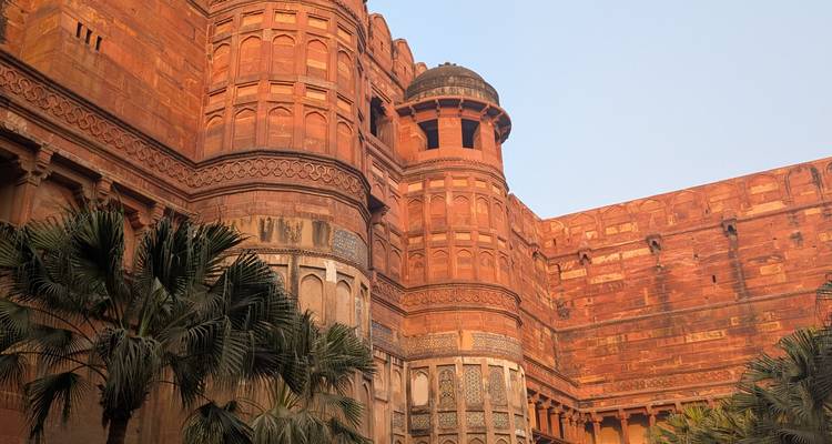Muros de arenisca roja de un fuerte histórico con palmeras.