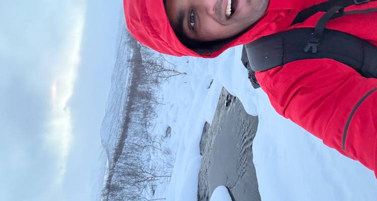 Persona con chaqueta roja parada en un paisaje nevado cerca de un arroyo.
