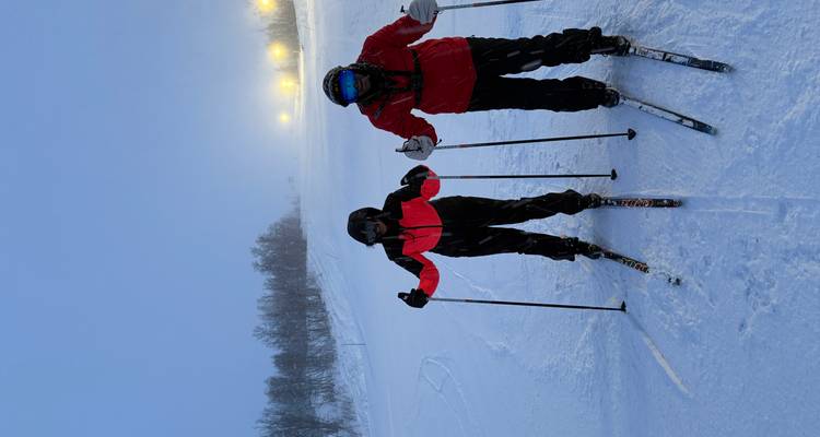 Dos personas con equipo de esquí paradas en una pendiente nevada.